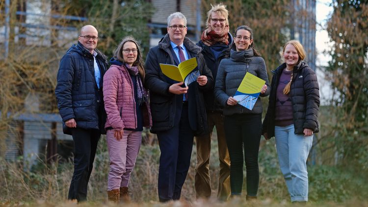 The group in the green in front of a university building, two people hold the climate protection concept in their hands. 