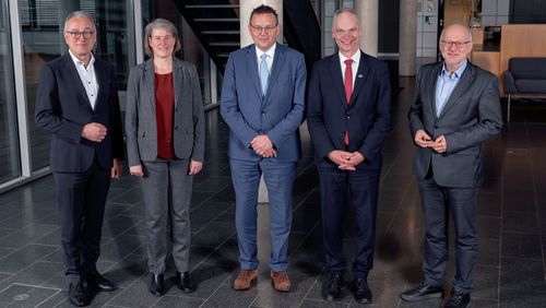 Fünf Personen stehen nebeneinander in einer Halle. 