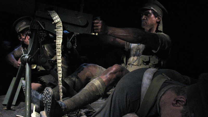 Das Bild zeigt eine Soldaten-Wachsfigur, die ein Maschinengewehr abfeuert. Um die Figur sind weitere Soldaten drapiert, offenbar ist mindestens einer von ihnen tot. Der MG-Schütze schaut grimmig.