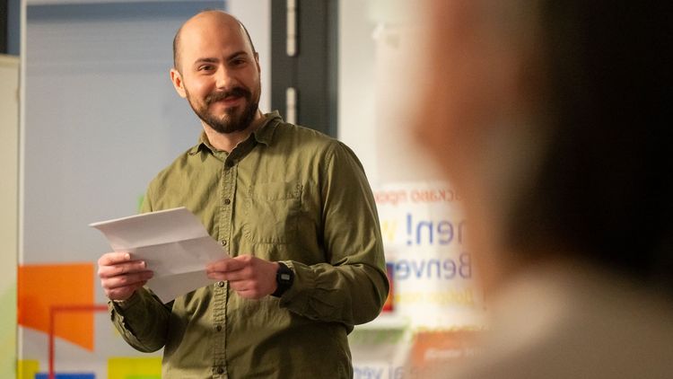The picture shows Matheus Silveira Mendes. He is holding a piece of paper in his hand while giving a speech. He smiles at the audience.