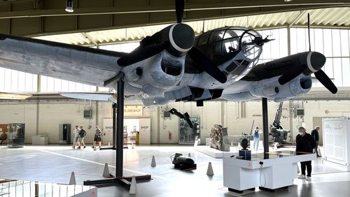 The picture shows a model of a bomber in a large museum hall. The aircraft's bomb bay is open and some bombs are falling out. The frieze fragment mentioned in the text can be seen in the background. Some visitors are standing in the hall and look at the exhibition.