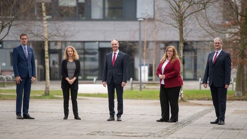 The five people stand at a distance in front of the A5 building of the university.