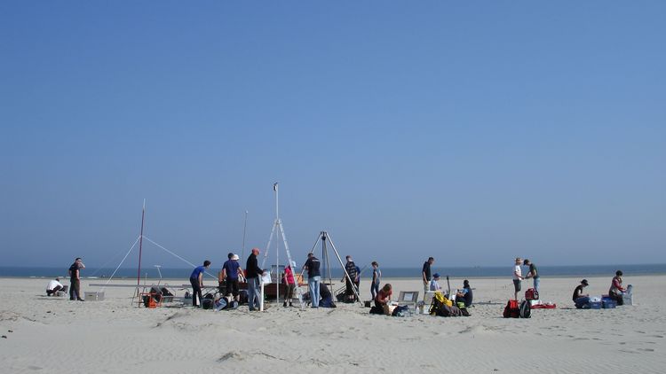 Viele Personen führen Messungen auf einem Sandstrand durch.