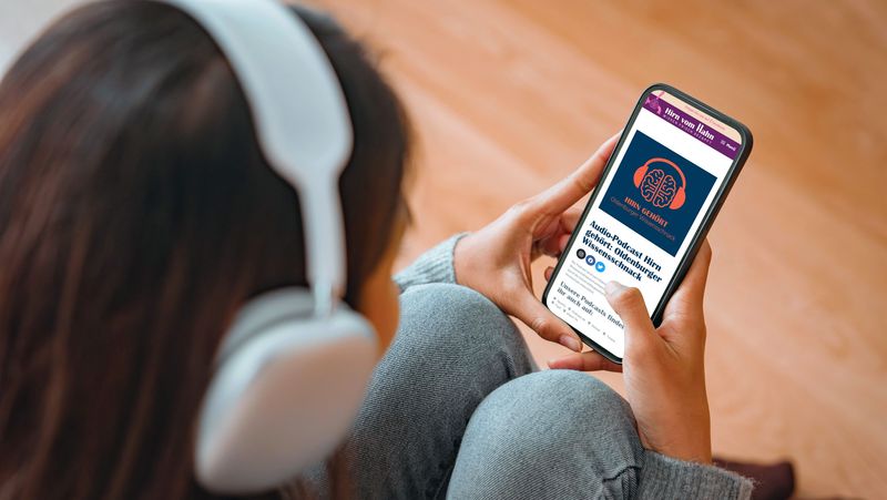 Frau mit Kopfhörern hält Handy in der Hand auf dem der Podcast "Hirn vom Hahn" angezeigt wird.